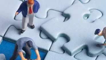 Miniature figures working on large puzzle pieces