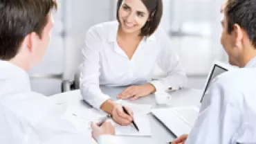 Three people in a meeting, discussing paperwork and smiling.