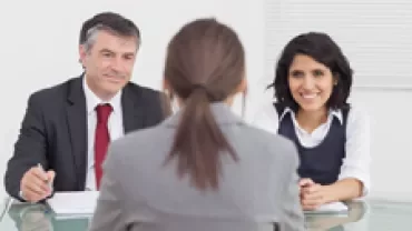 Two people interviewing a person sitting at a table.