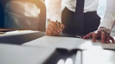 Person in formal attire signing a document at a desk.