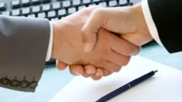 Hands shaking over a desk with a keyboard and a pen on a document.