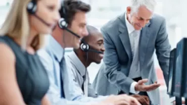 Business team at workstations with headsets, collaborating with a supervisor.
