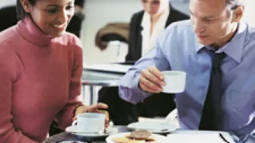 Two people enjoying coffee and conversation at a table with documents in an office setting.