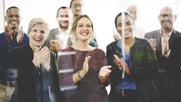 Group of people smiling and clapping in an office setting.