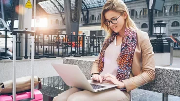 Person sitting on a bench using a laptop at a train station.
