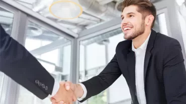 Person in a suit smiling and shaking hands in a modern office setting.