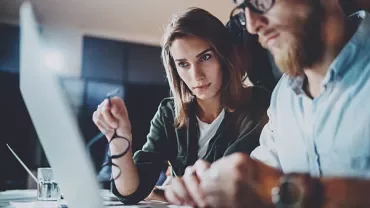 Two people working together at a computer, focused and collaborating.