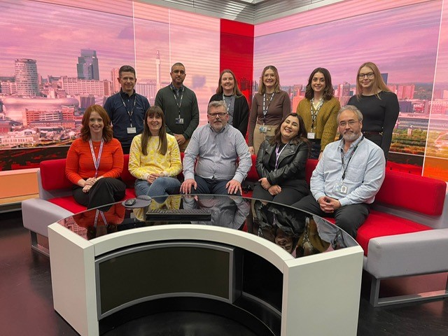 BBC Team together near a sofa getting ready for the news