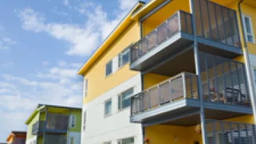 Modern yellow apartment building with balconies under a blue sky.