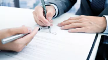 Close-up of hands signing a document at a desk.