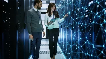 Two professionals examine a digital network interface in a server room.