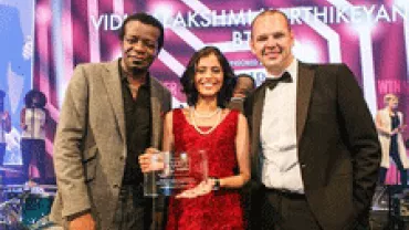 Three people smiling on stage with an award.