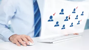 Person using computer with icons of people and checkmarks on screen.